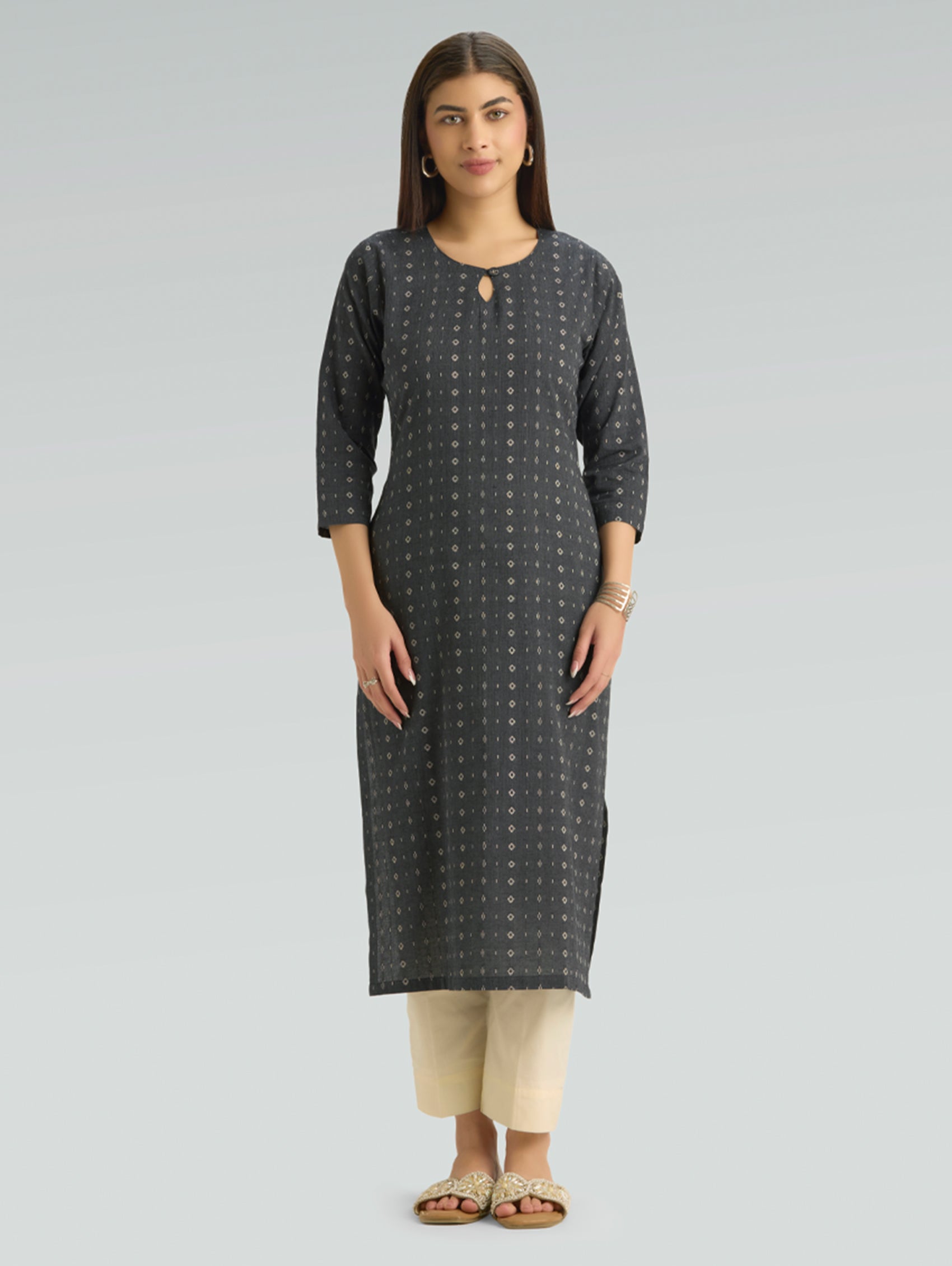 Woman wearing a dark grey patterned kurta with  side slit and beige pants on a light grey background