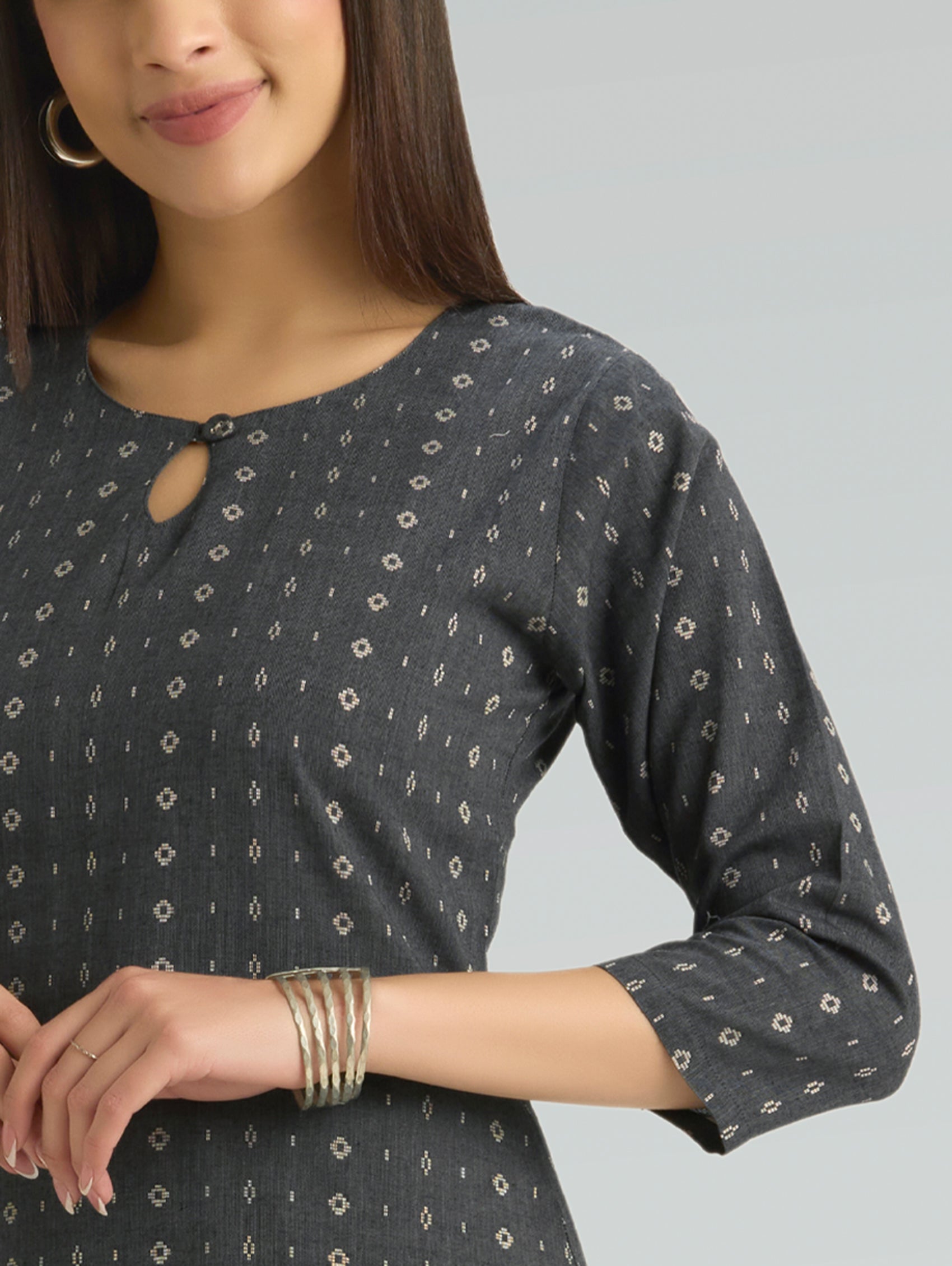 Woman wearing a dark grey patterned dress with long sleeves and keyhole neck on a light grey background