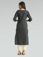 Woman wearing a black patterned kurta with white pants on a gray background