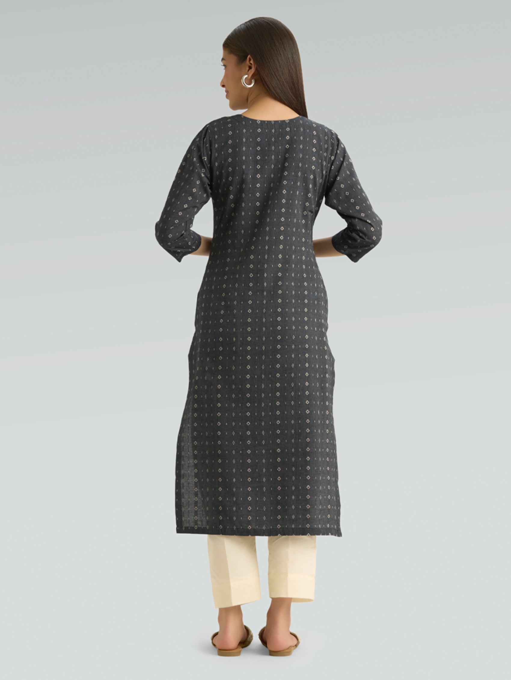 Woman wearing a black patterned kurta with white pants on a gray background