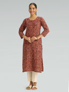 Woman wearing a red Kalamkari-patterned kurta with front and side slit white pants on a grey background