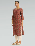 Woman wearing a red Kalamkari-patterned kurta with front and side slit white pants on a grey background