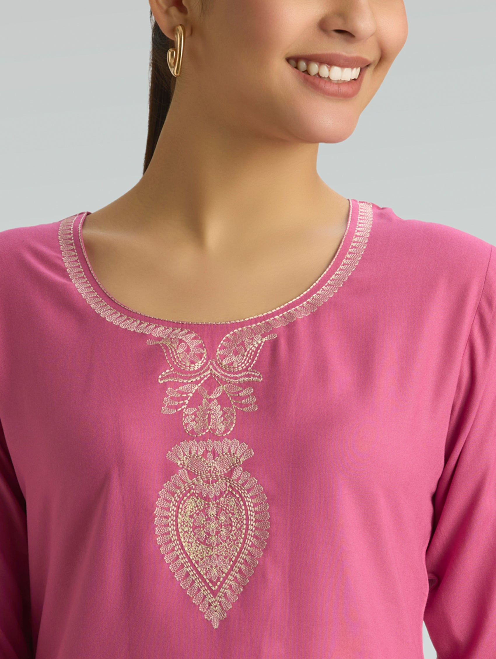 Close-up of a pink kurta with intricate white embroidery on a plain background