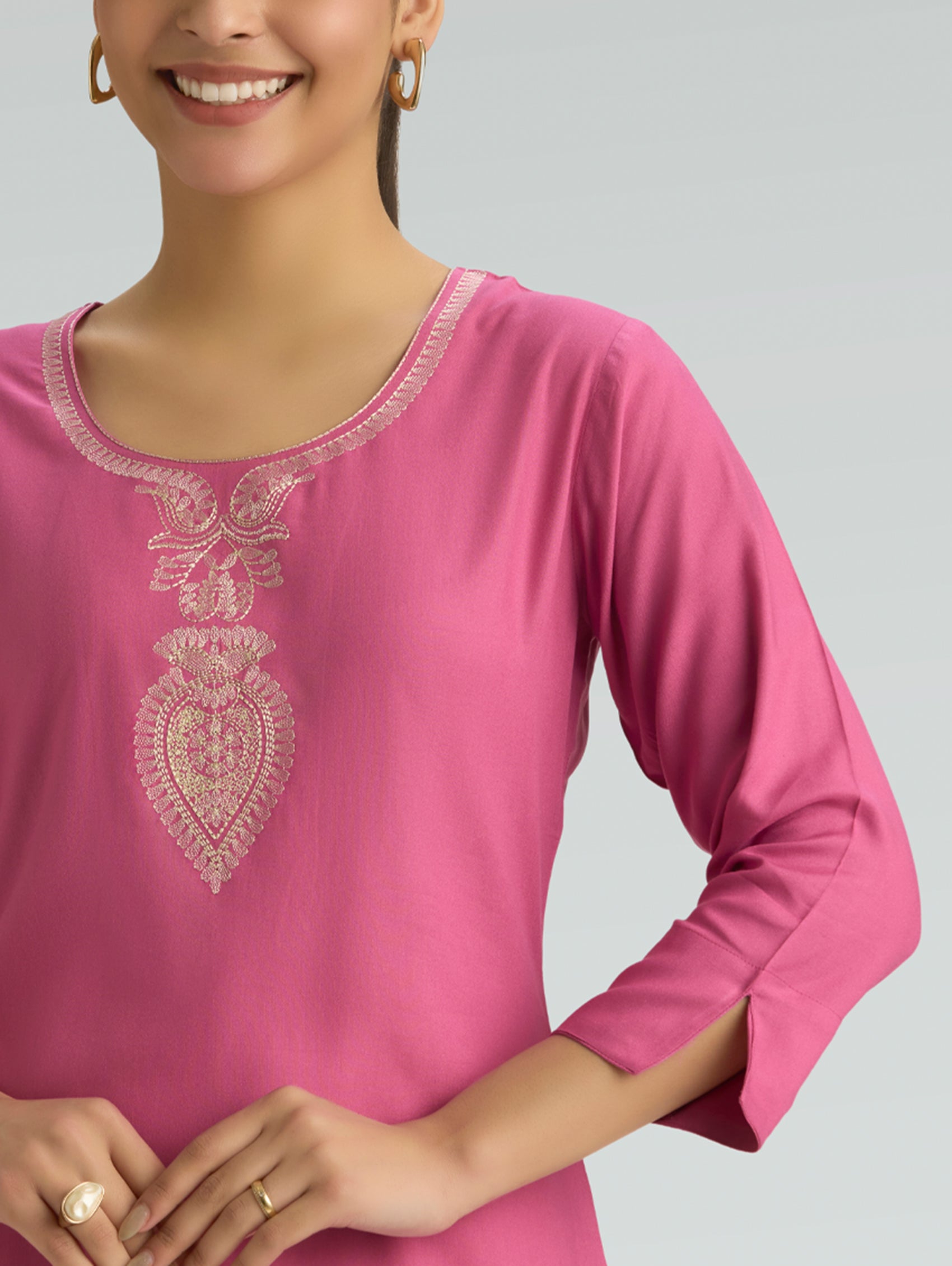 Woman wearing a pink top with intricate white embroidery on a gray background