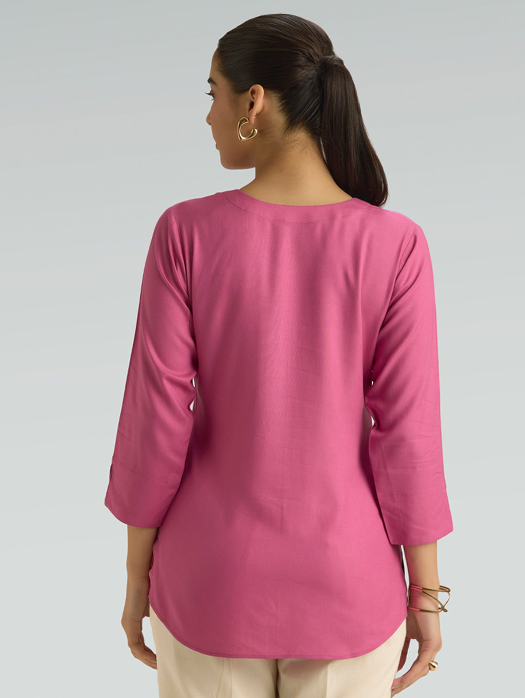 Woman wearing a pink long-sleeve top on a gray background