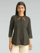Woman wearing a dark green blouse with floral embroidery on a gray background