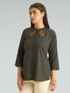 Woman wearing a dark green blouse with floral embroidery on a gray background