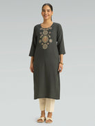 Woman wearing a dark green kurta with embroidery on a gray background