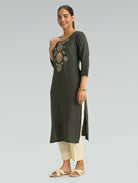 Woman wearing a dark green kurta with embroidery on a light gray background