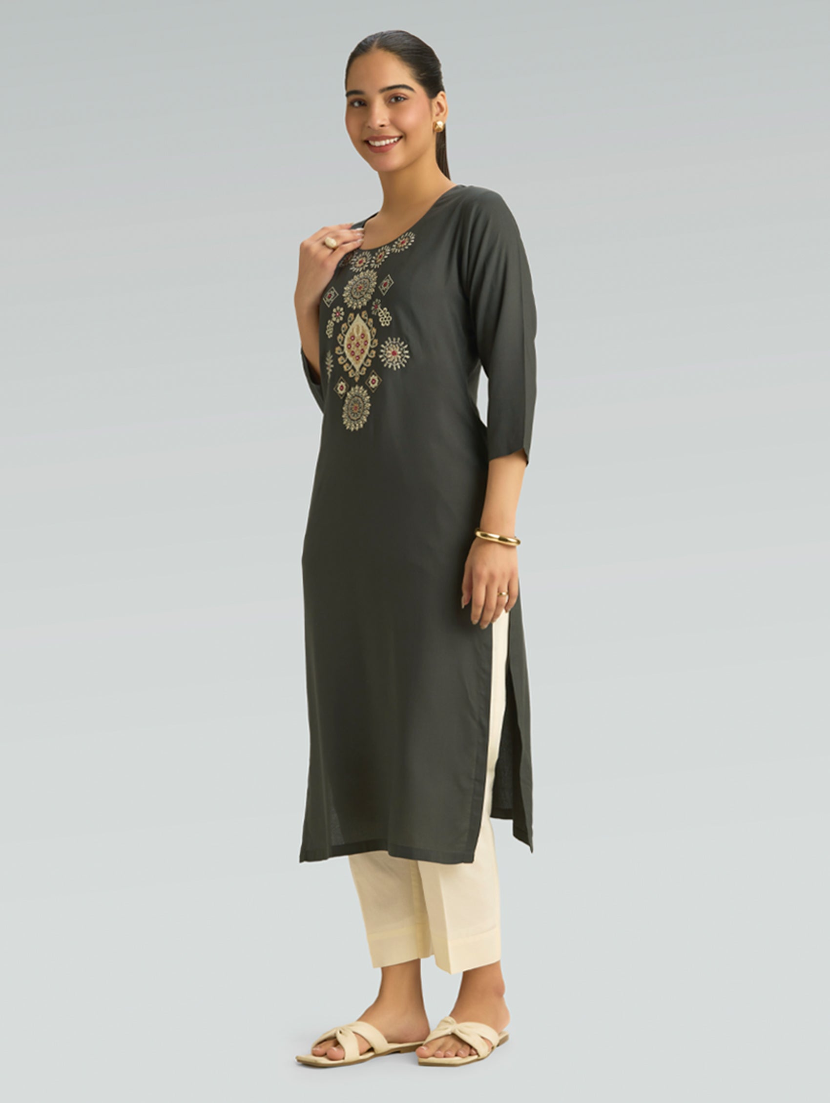Woman wearing a dark green kurta with embroidery on a light gray background