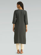 Woman wearing a dark gray kurta with white pants on a light gray background