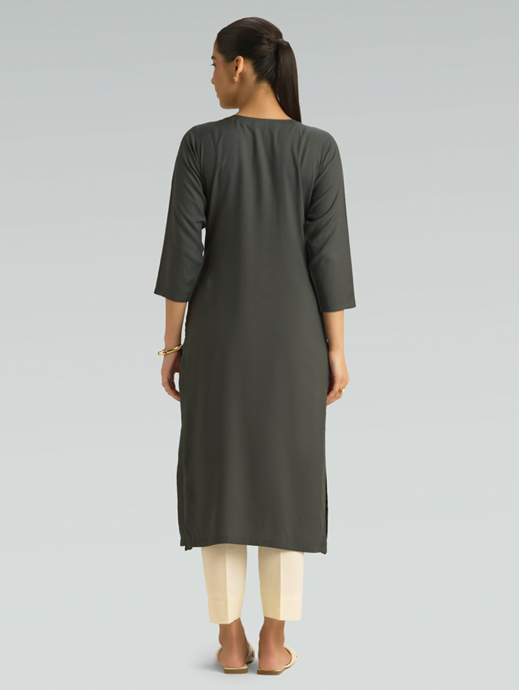 Woman wearing a dark gray kurta with white pants on a light gray background