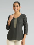 Woman wearing a black top with an embroidered neckline on a gray background