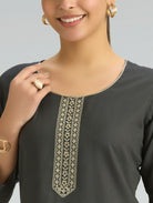 Woman wearing a black top with intricate white embroidery on a gray background