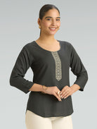 Woman wearing a dark gray long-sleeve top with decorative embroidery on a plain background