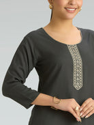 Woman wearing a dark gray long-sleeve top with decorative embroidery on a light gray background