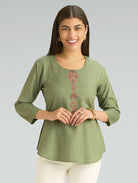Woman wearing a green top with a decorative pattern on a gray background