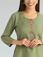 Woman wearing a green dress with floral embroidery on a plain background