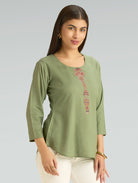 Woman wearing a green top with floral embroidery on a gray background
