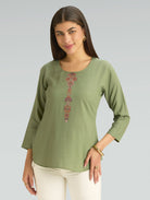 Woman wearing a green top with a decorative pattern on a gray background