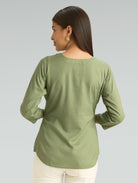 Woman wearing a green long-sleeve top on a gray background