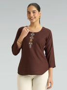 Woman wearing a brown top with decorative elements on a gray background