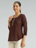 Woman wearing a brown top with floral embellishments on a gray background