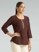 Woman wearing a brown blouse with floral embroidery on a gray background