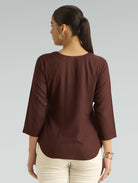 Woman wearing a brown blouse with three-quarter sleeves on a gray background