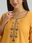 Close-up of a mustard yellow top with intricate black and gold embroidery on a plain background