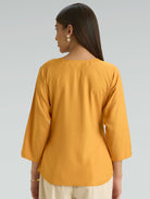Woman wearing a mustard yellow top on a gray background