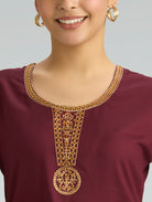 Close-up of a maroon top with gold embroidery on a plain background