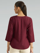 Woman wearing a maroon top with three-quarter sleeves on a gray background