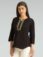 Woman wearing a black top with gold embroidery on a gray background