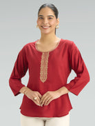 Woman wearing a red top with gold embroidery on a gray background
