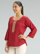 Woman wearing a red top with gold embroidery on a gray background