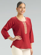 Woman wearing a red blouse with gold embroidery on a gray background