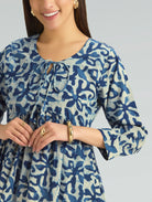 Woman wearing a blue and white patterned dress with jewelry on a gray background