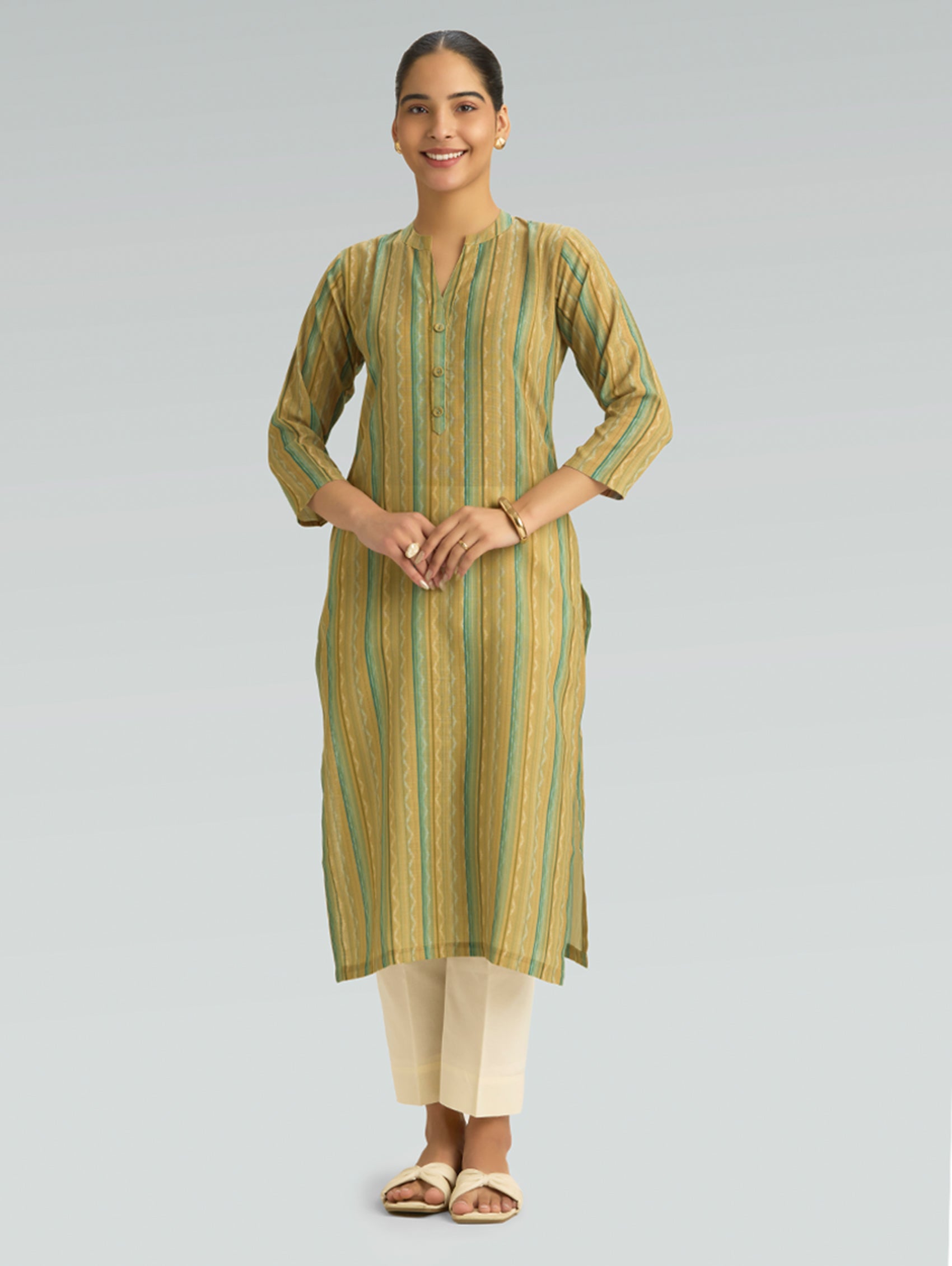 Woman wearing a green and beige striped kurta with white pants on a gray background