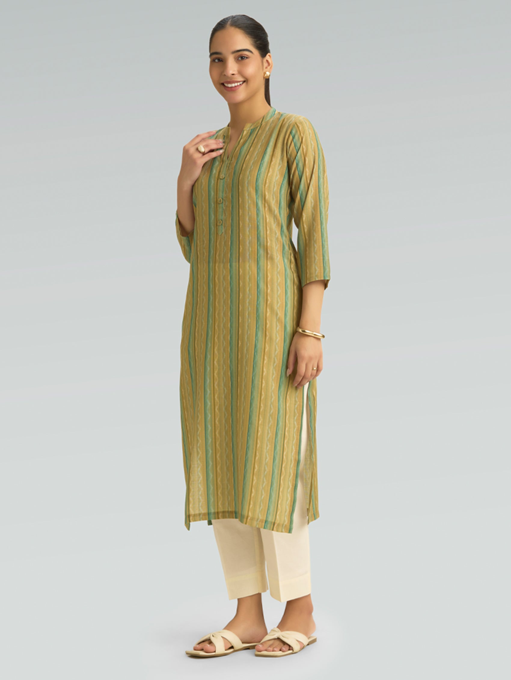 Woman wearing a green and beige striped kurta with white pants on a gray background
