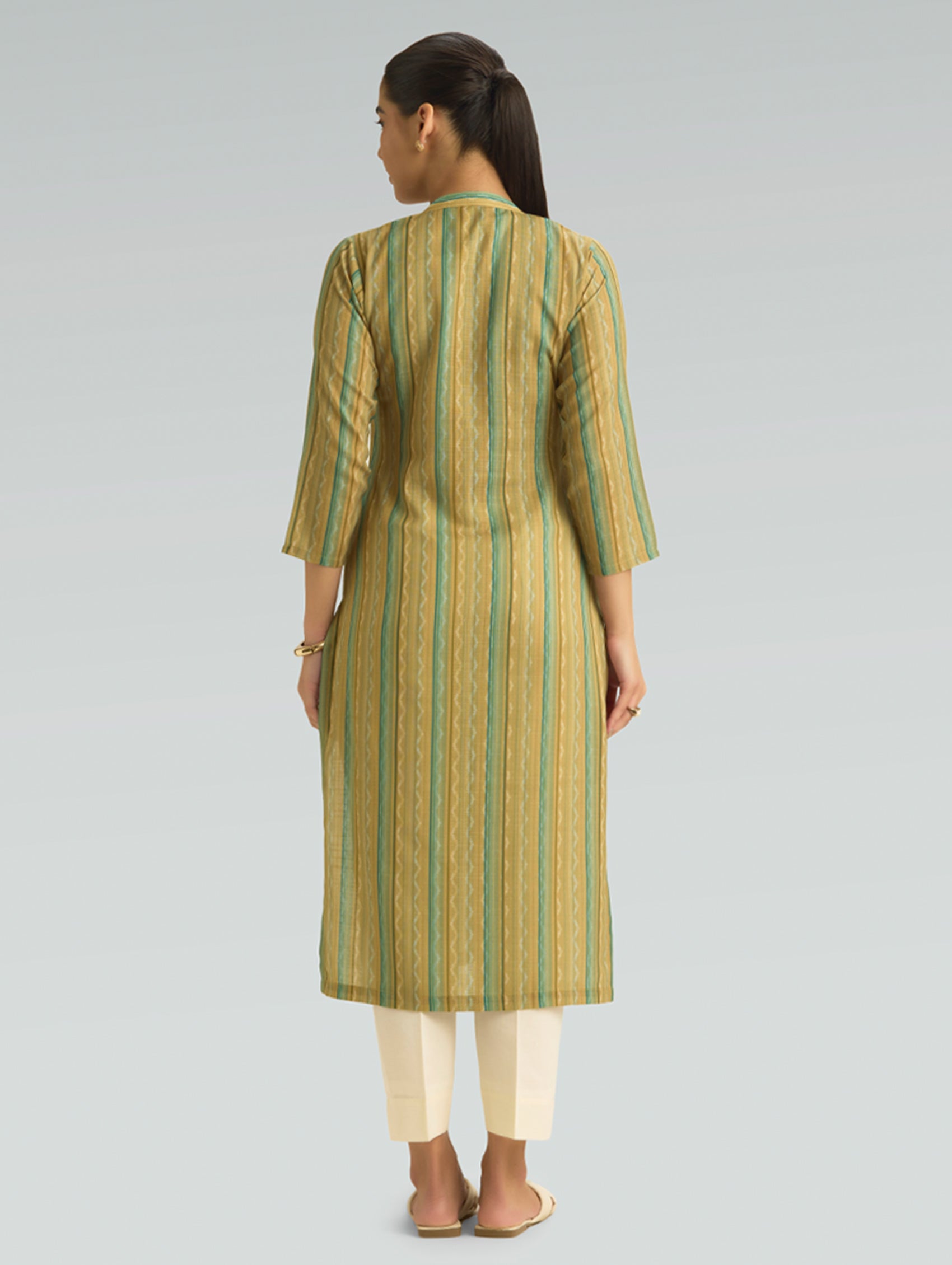 Woman wearing a green and beige striped kurta with white pants on a gray background