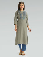 Woman wearing a long green patterned dress with blue accents on a gray background