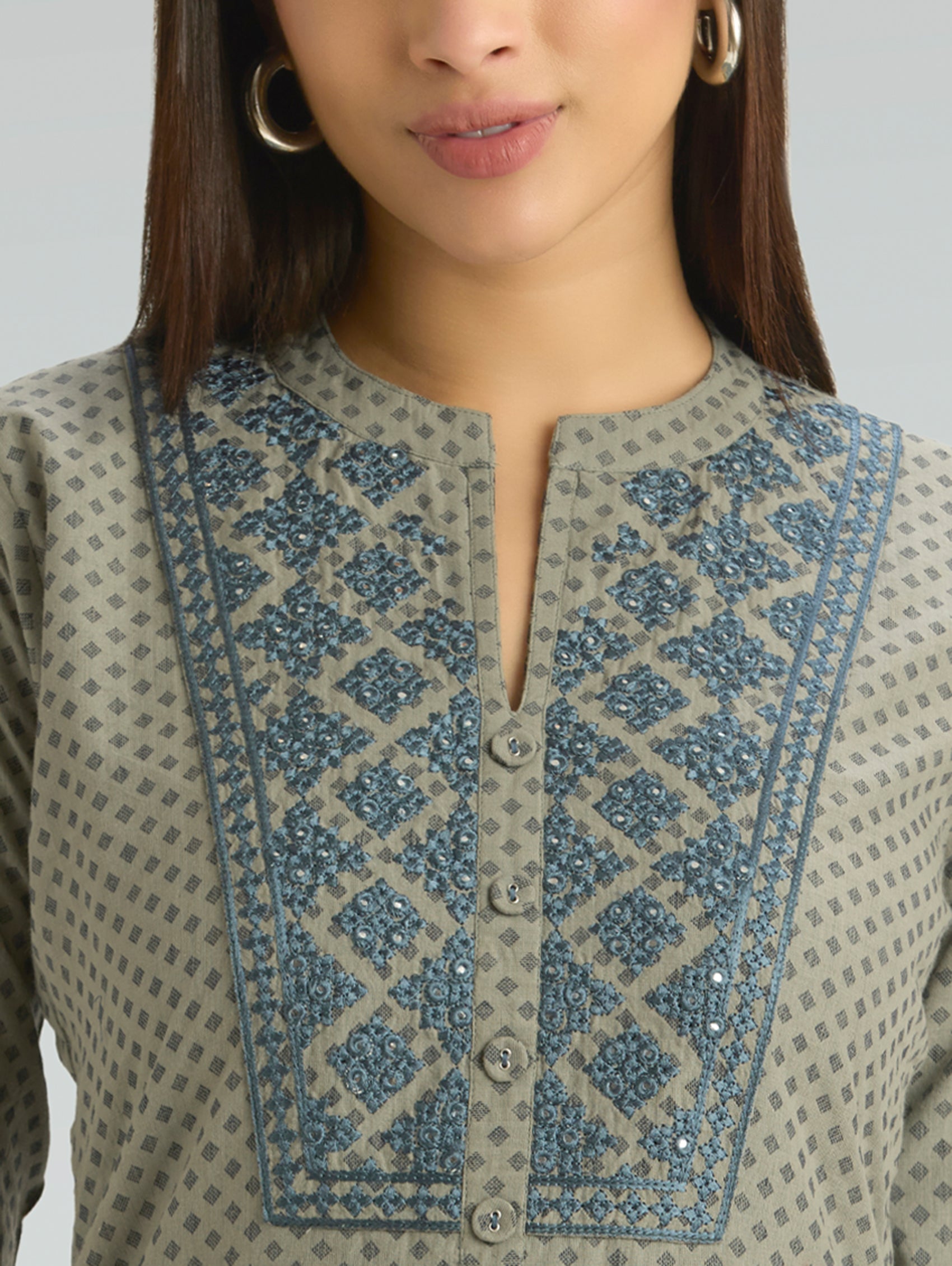 Close-up of a person wearing a traditional outfit with intricate embroidery on a plain background