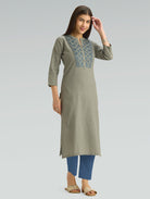 Woman wearing a green kurta with blue embroidery on a gray background