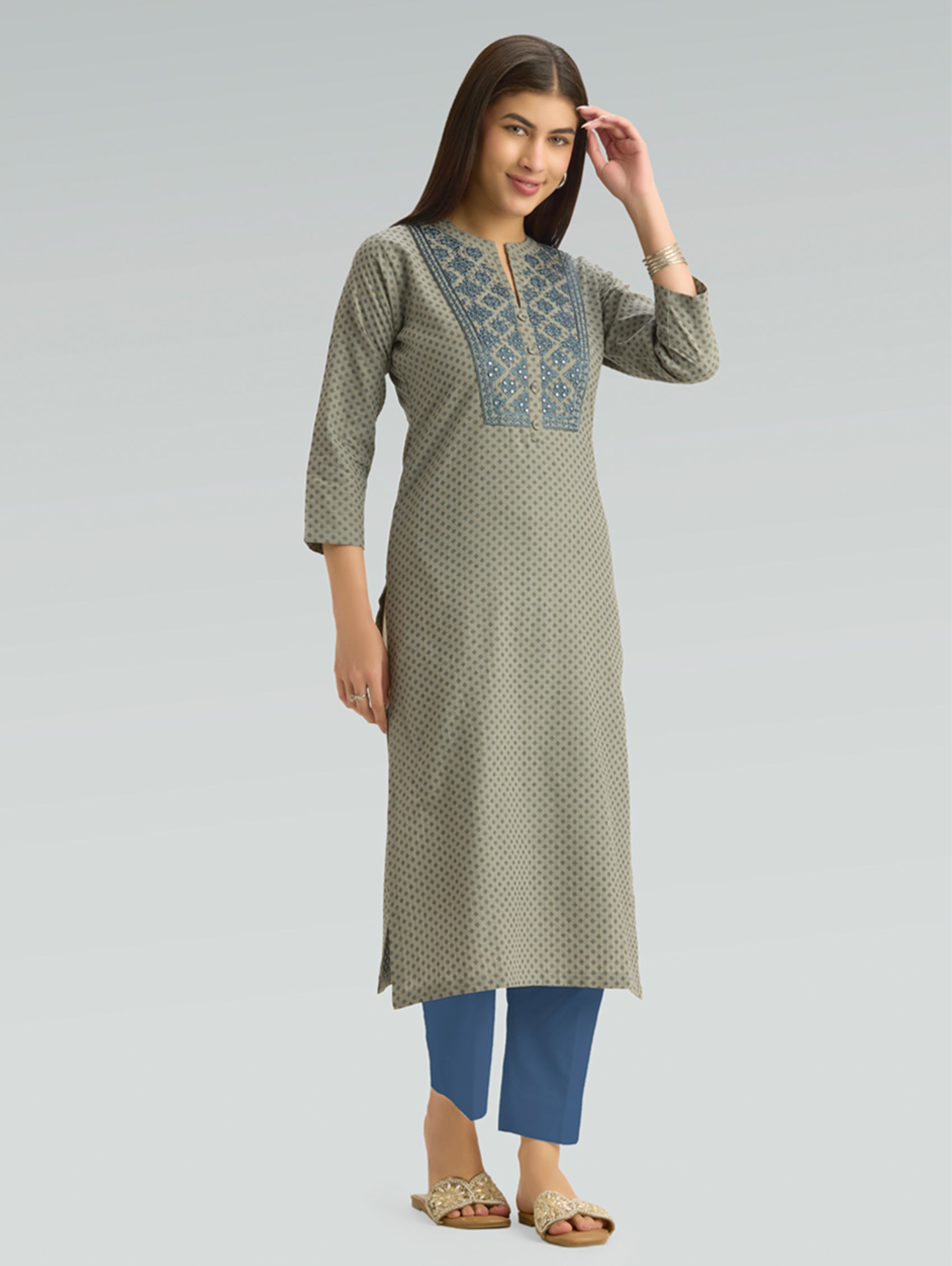 Woman wearing a green kurta with blue embroidery on a gray background