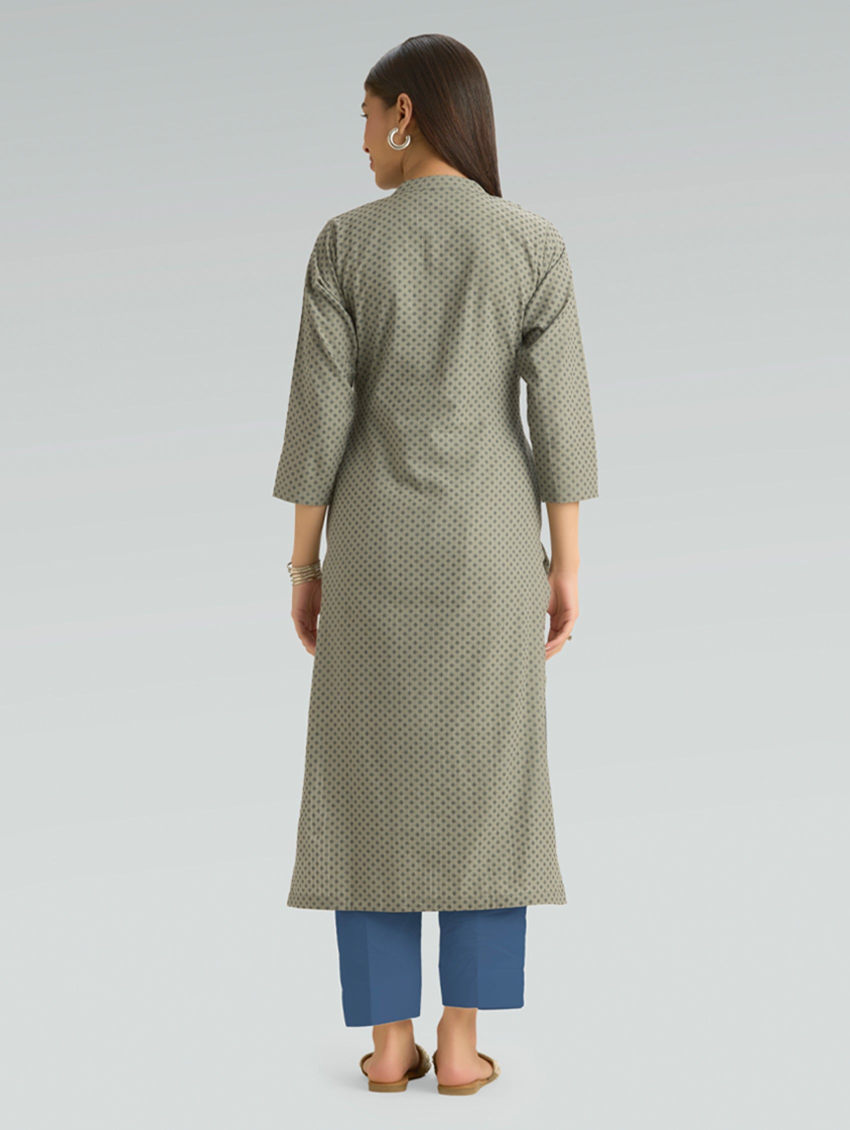 Woman wearing a green patterned kurta with blue pants on a light gray background