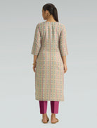 Woman wearing a patterned kurta with pink pants on a gray background