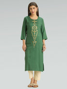 Woman wearing a green kurta with gold embroidery on a gray background