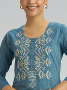 Woman wearing a blue embroidered top with a plain background