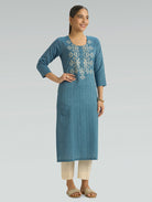 Woman wearing a blue embroidered kurta with beige pants on a gray background